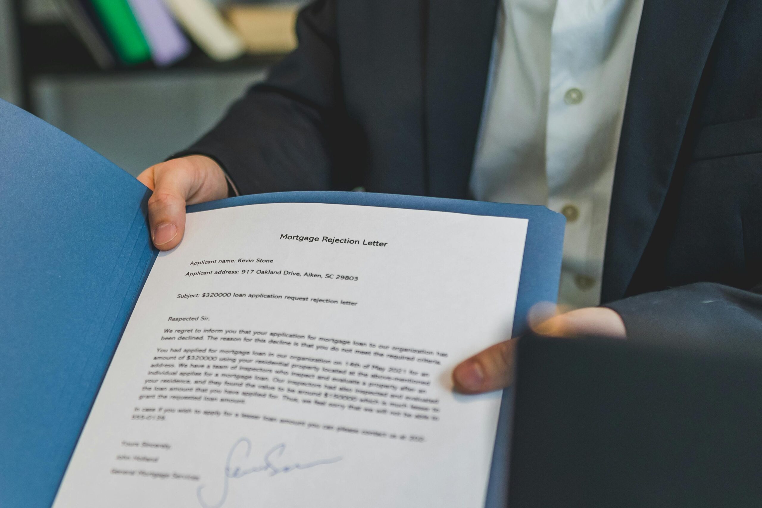 Close-up view of a person holding a mortgage rejection letter in a folder, indoors.